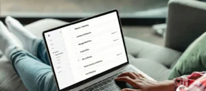 Person using a laptop to access a GoDaddy account dashboard. The screen displays a list of services including Websites + Marketing, Commerce & Payments, Managed WordPress, Email & Office, and SSL Certificates.